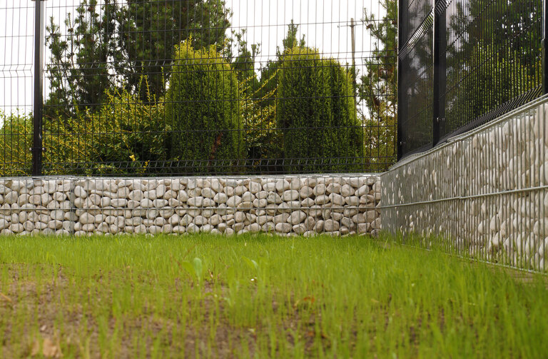 Gartenzaun. Ecke aus Gabionen, gefüllt mit weißen Kieselsteinen.