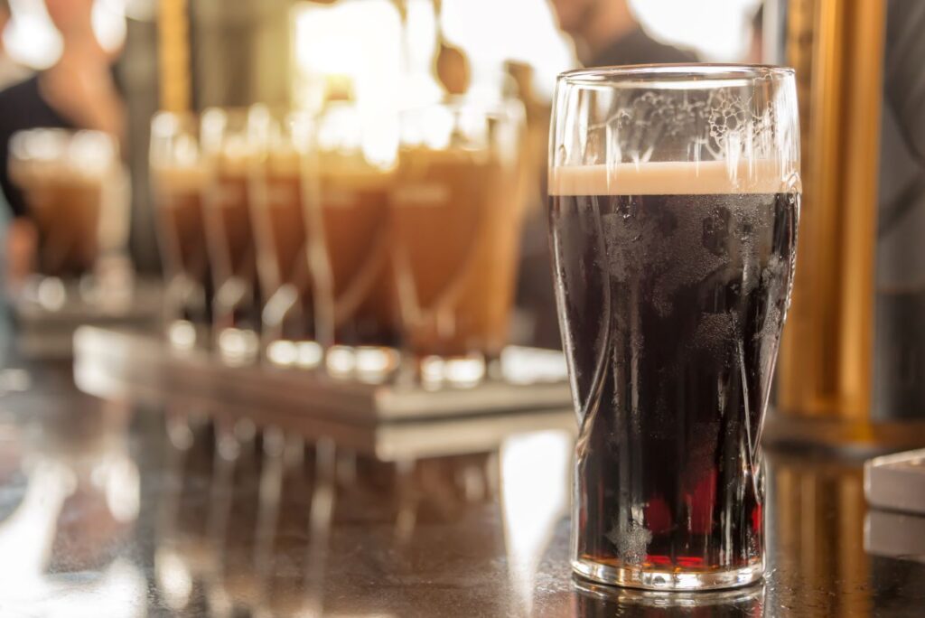 Ein Glas Guinness Bier mit cremigem Schaum steht im Fokus auf einer Theke, im Hintergrund weitere frisch gezapfte Biere.