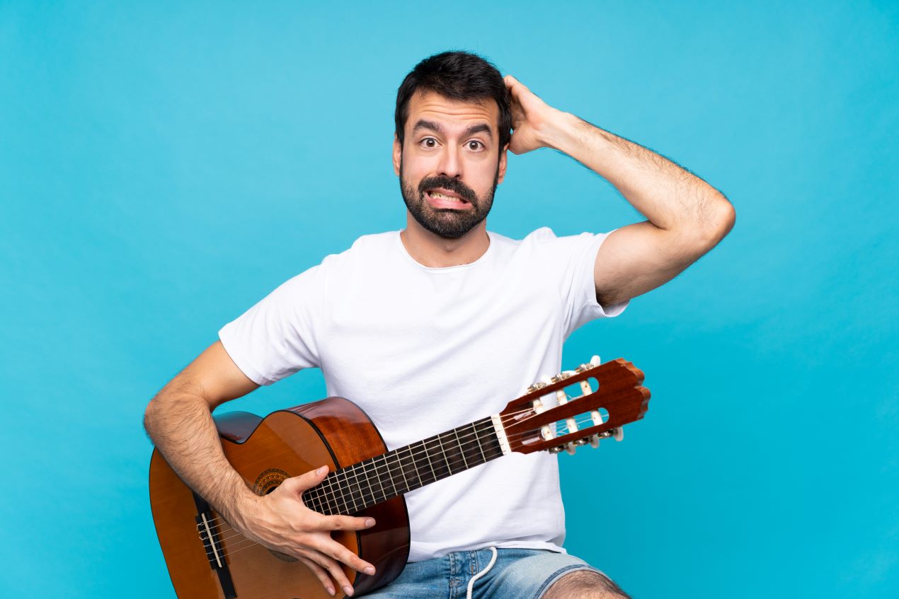 Frustrierter Mann mit Gitarre, der unter schlechter Raumakustik leidet, perfekte Lösung durch Akustikpaneele Holz