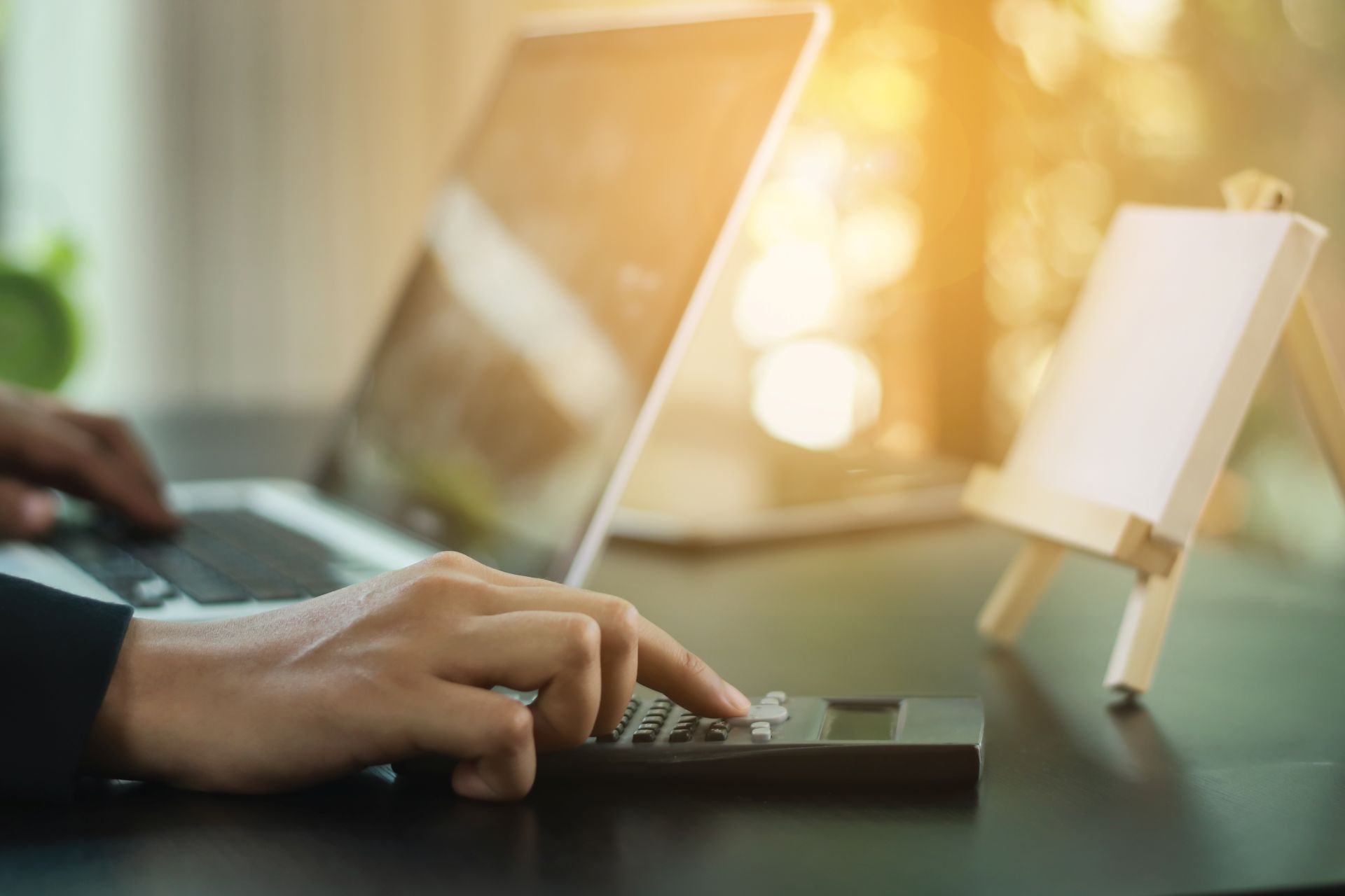 Person kalkuliert Energiekosten am Laptop mit Taschenrechner